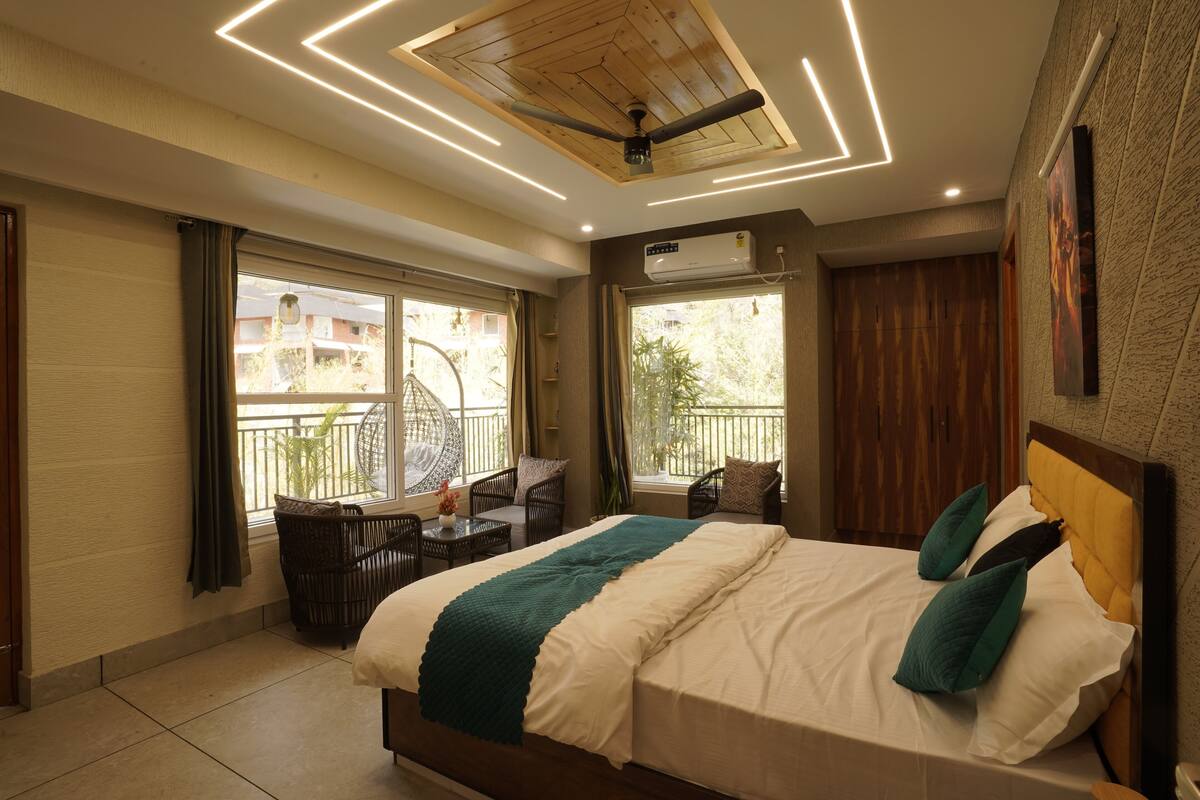 A bedroom with a bed, a ceiling fan, a window, a balcony, and a seating area with a table and chairs.
