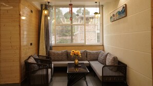 Una habitación con pared de madera, una ventana con cortinas, un sofá, dos sillones, una mesa con un jarrón y un cuadro en la pared.