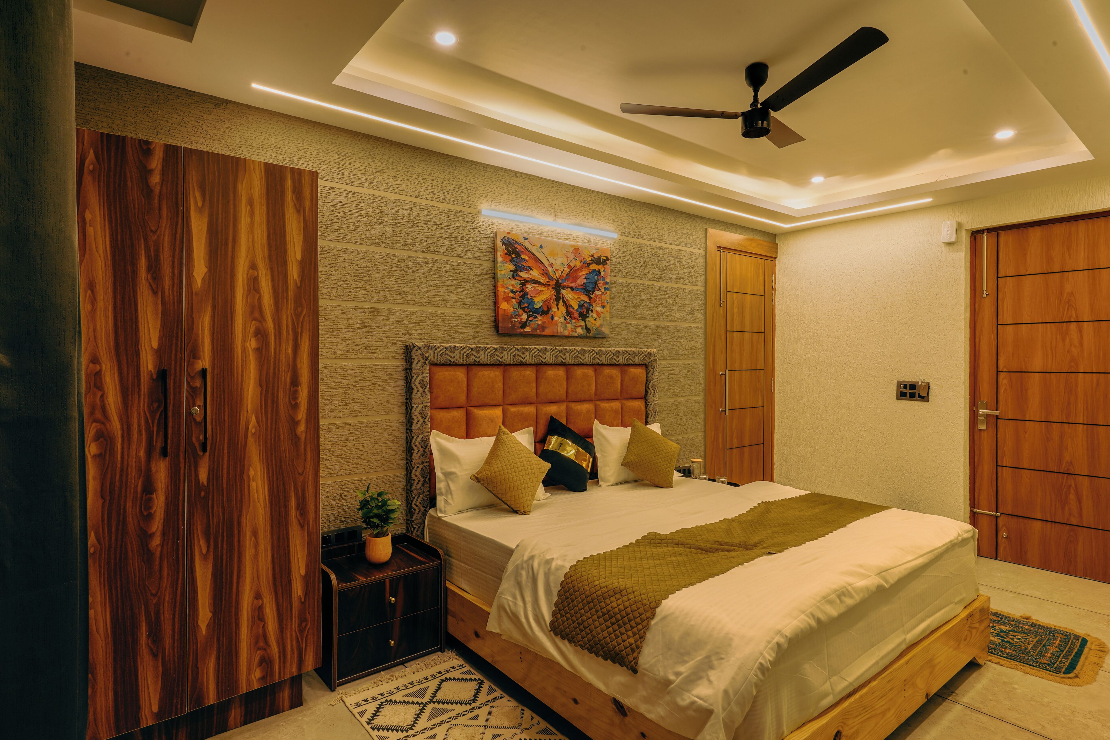 A bedroom with a bed, a ceiling fan, a wall-mounted painting, and a wooden wardrobe.