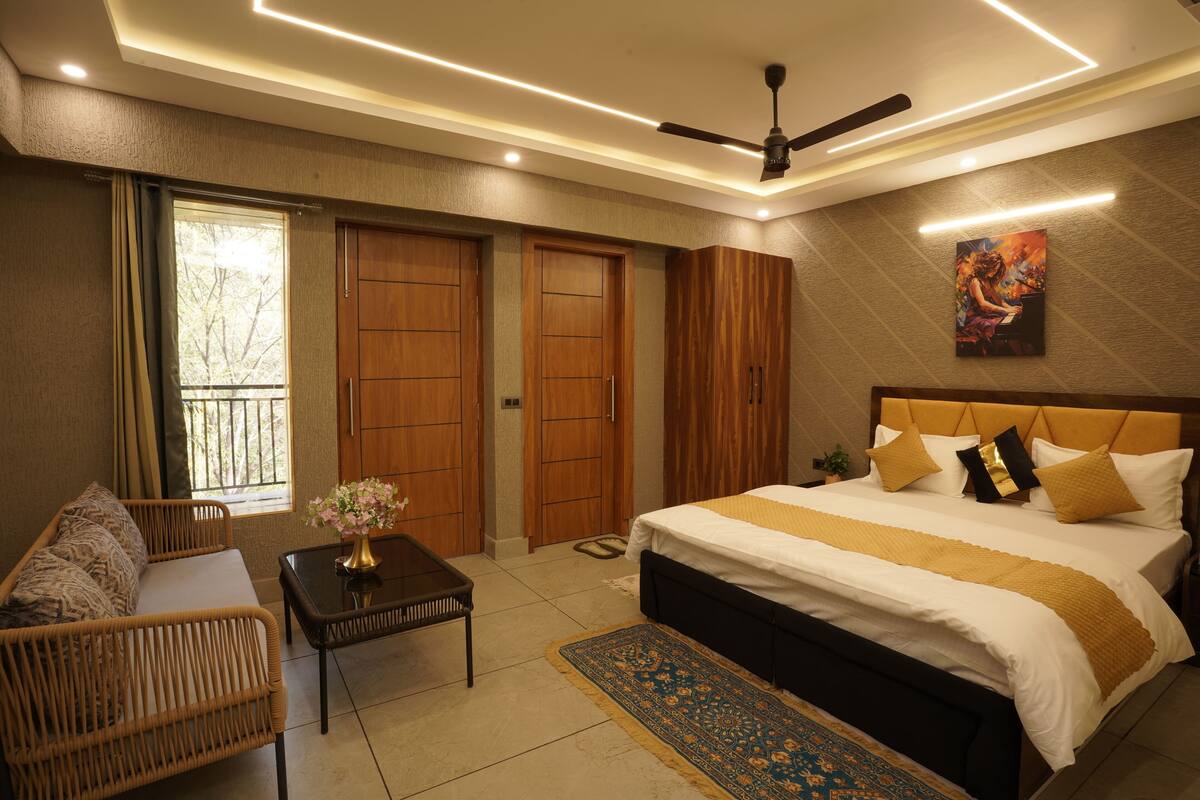 A bedroom with a bed, a sofa, a table, a ceiling fan, and a window.