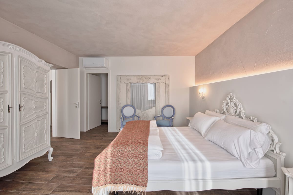 A bedroom with a large bed, a wardrobe, a mirror, and a door leading to another room.