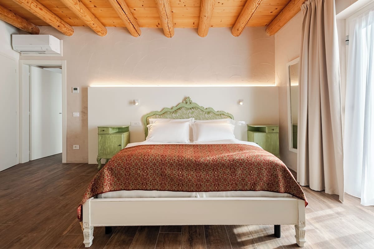 A bedroom with a wooden ceiling, a bed with a patterned bedspread, bedside tables, and a green cabinet.
