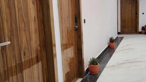 A hallway with wooden doors, potted plants, and a marble floor. - Patram Haveli (Roorkee)