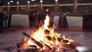 A fire pit with logs, surrounded by a brick border, under string lights. - Patram Haveli (Roorkee)