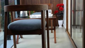 A modern interior with a wooden chair, a dining table, and a potted plant with red flowers. - The Avis Resort and Homestay (Idukki)