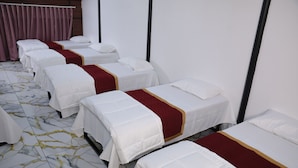 A hotel room with four single beds, each with a white bedspread and a red accent. The room has a marble-patterned floor and white walls. - The Avis Resort and Homestay (Idukki)