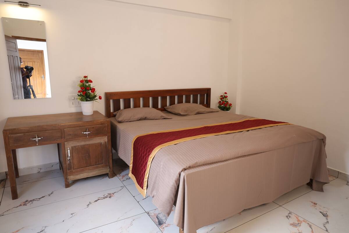 A bedroom with a wooden bed, a nightstand, a mirror, and a vase with flowers.