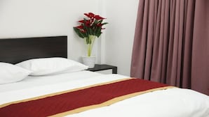 A neatly made bed with white bedding, a red and gold accent, a potted plant with red flowers, and a dark headboard. - The Avis Resort and Homestay (Idukki)