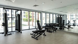 Un gimnasio con equipo de ejercicio, ventanas amplias y vistas a edificios.