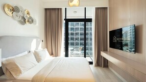 Habitación de hotel con una cama grande, un televisor montado en la pared y vistas de la ciudad a través de grandes ventanales.