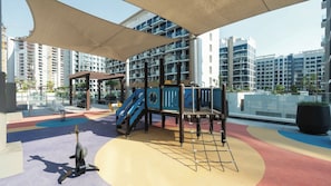 Un parque infantil con estructuras para escalar y toboganes, rodeado de edificios modernos.