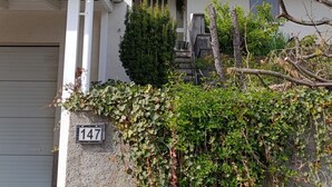 Una casa de dos pisos con techo rojo, paredes blancas y un pequeño porche.