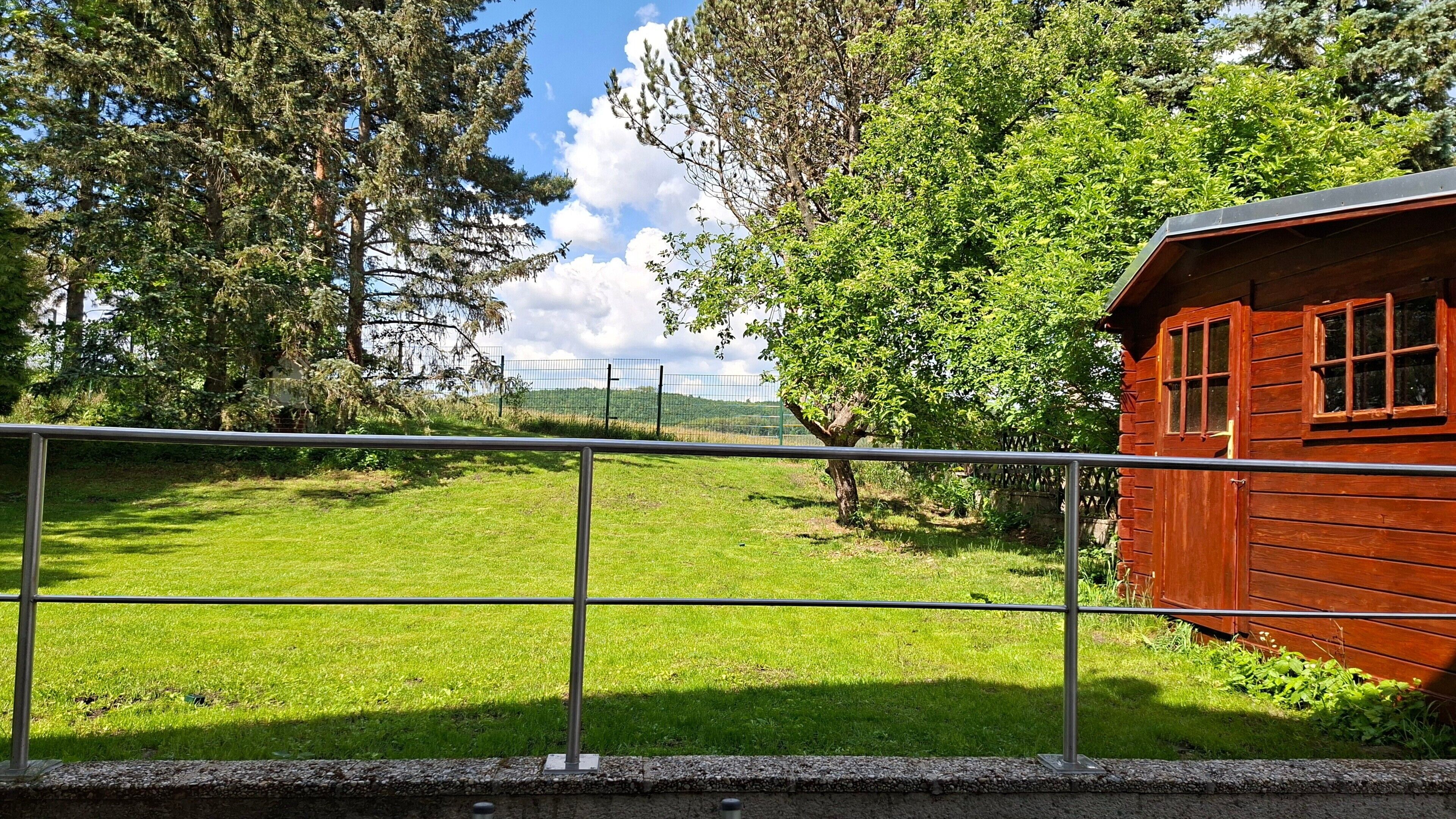 A fenced outdoor area with a wooden cabin, a grassy field, and trees.