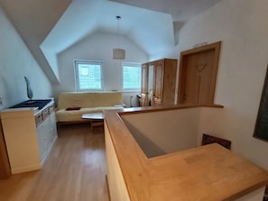 Ein Loft-Zimmer mit schrägem Dach, einer Couch, einer hölzernen Bank, einer kleinen Küchenzeile und einer Tür mit der Aufschrift 'HOLLYWOOD'.