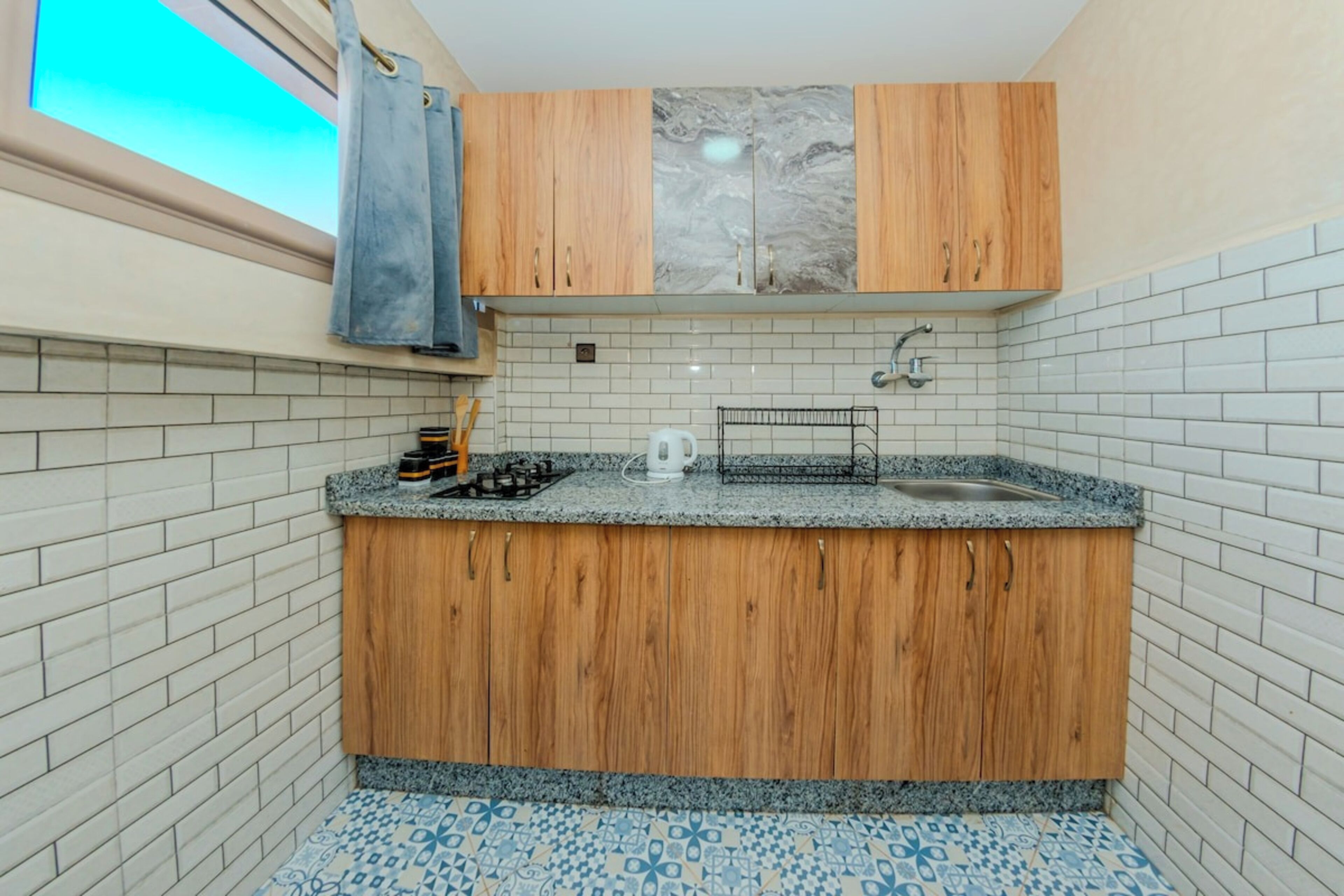 Een kleine keuken met houten kastjes, een granieten aanrechtblad en een vloer met een patroon.