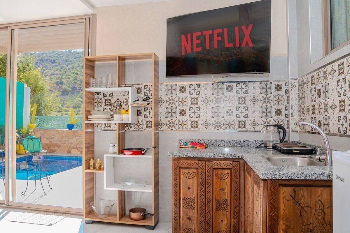 A modern kitchen with a built-in TV, a pool view, and a wooden cabinet.