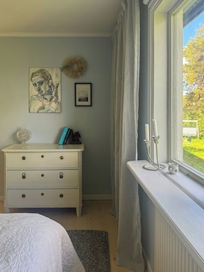 A bedroom with a bed, a dresser, a window with curtains, and artwork on the wall.