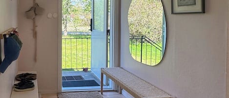 Una habitació amb una banca de fusta, una cistella de vimet, una porta que dóna a l'exterior i un quadre encarregat a la paret.
