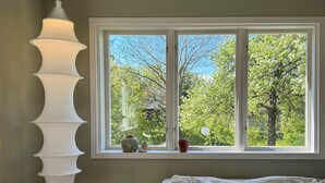 A room with a large window, a white table with a notebook, a beige sofa, and a tall white lamp.