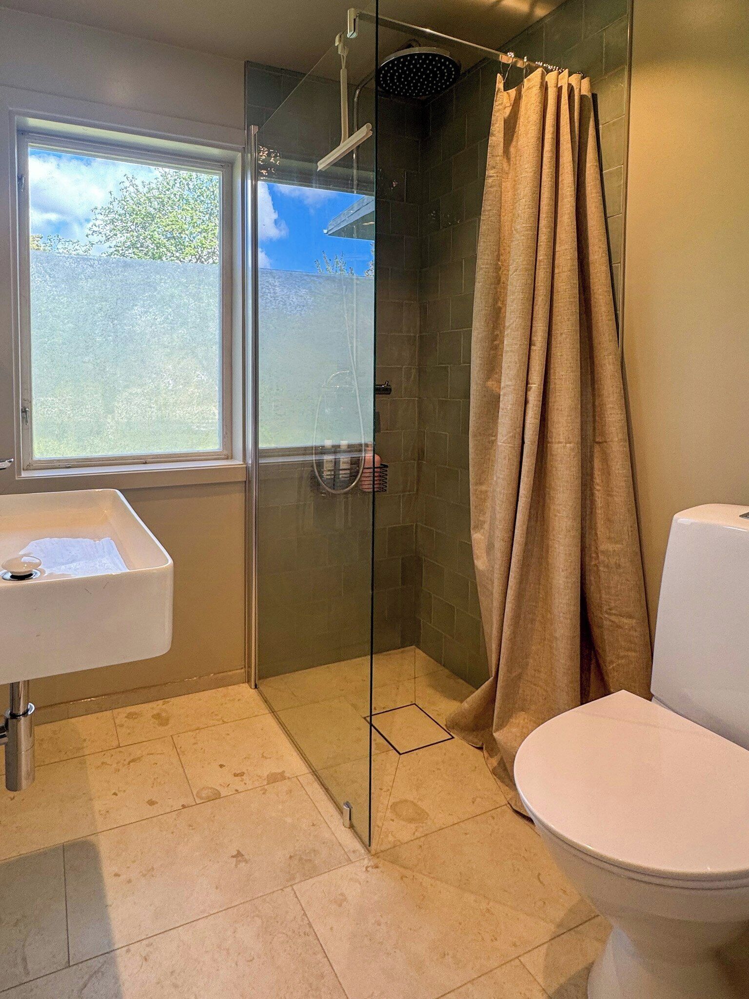 A bathroom with a glass-enclosed shower, a toilet, a sink, and a window.