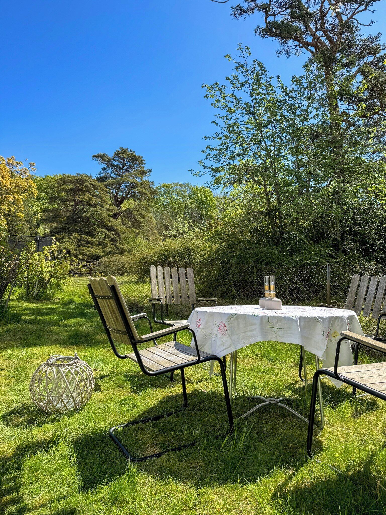 An outdoor dining area with a table and chairs, surrounded by greenery and trees.
