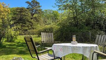 An outdoor dining area with a table and chairs, surrounded by greenery and trees.