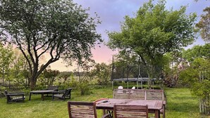 A grassy outdoor area with wooden furniture, including benches and a table, surrounded by trees.