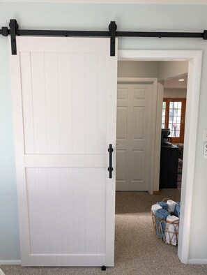 A white sliding barn door with black hardware, leading to a room with a white door and a window. - NEW!  Villa Adonis - Lakefront, Dog-Friendly, and Gorgeous!  Includes NEW 6-PERSON HOT TUB, Central Air, and Water Toys! (National City)