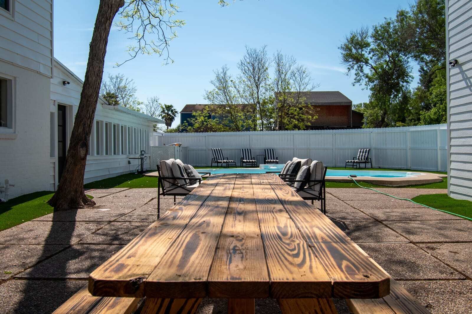 A backyard with a wooden picnic table, lounge chairs, and a swimming pool.
