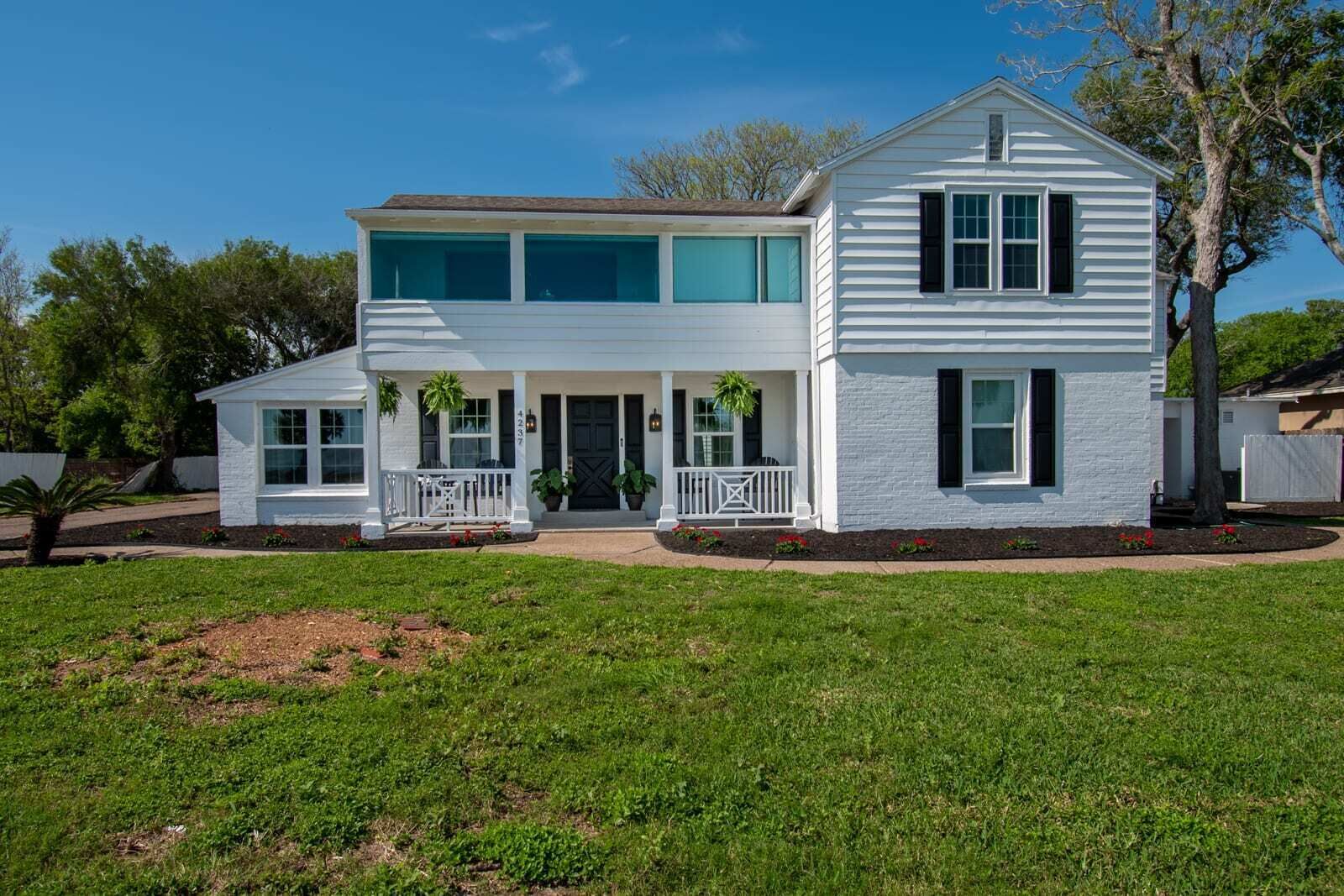 A two-story white house with a front porch, a garage, and a well-maintained lawn.