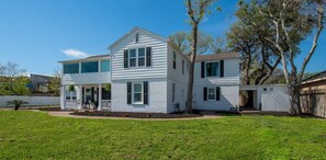 Uma casa branca de dois andares com varanda, quintal cercado e árvores.
