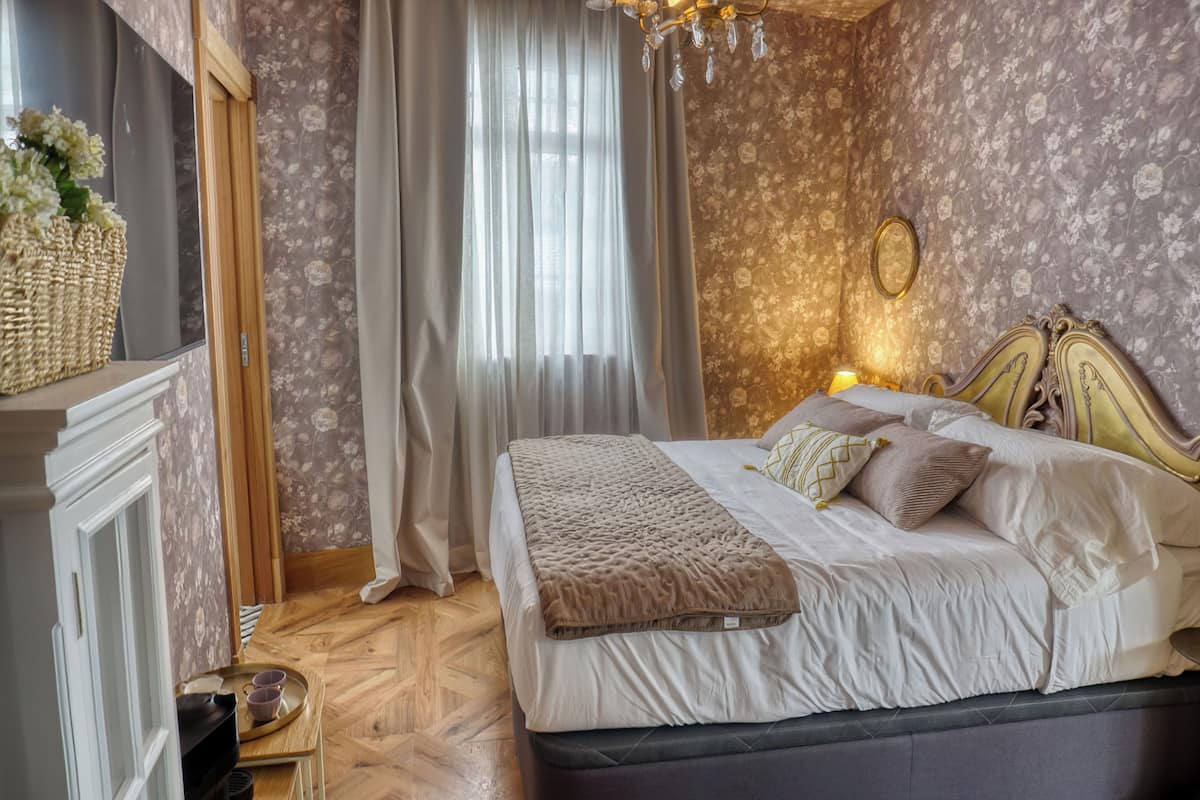 A bedroom with a bed, curtains, a chandelier, and a mirror.