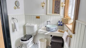 A bathroom with a toilet, sink, mirror, and a trash bin.