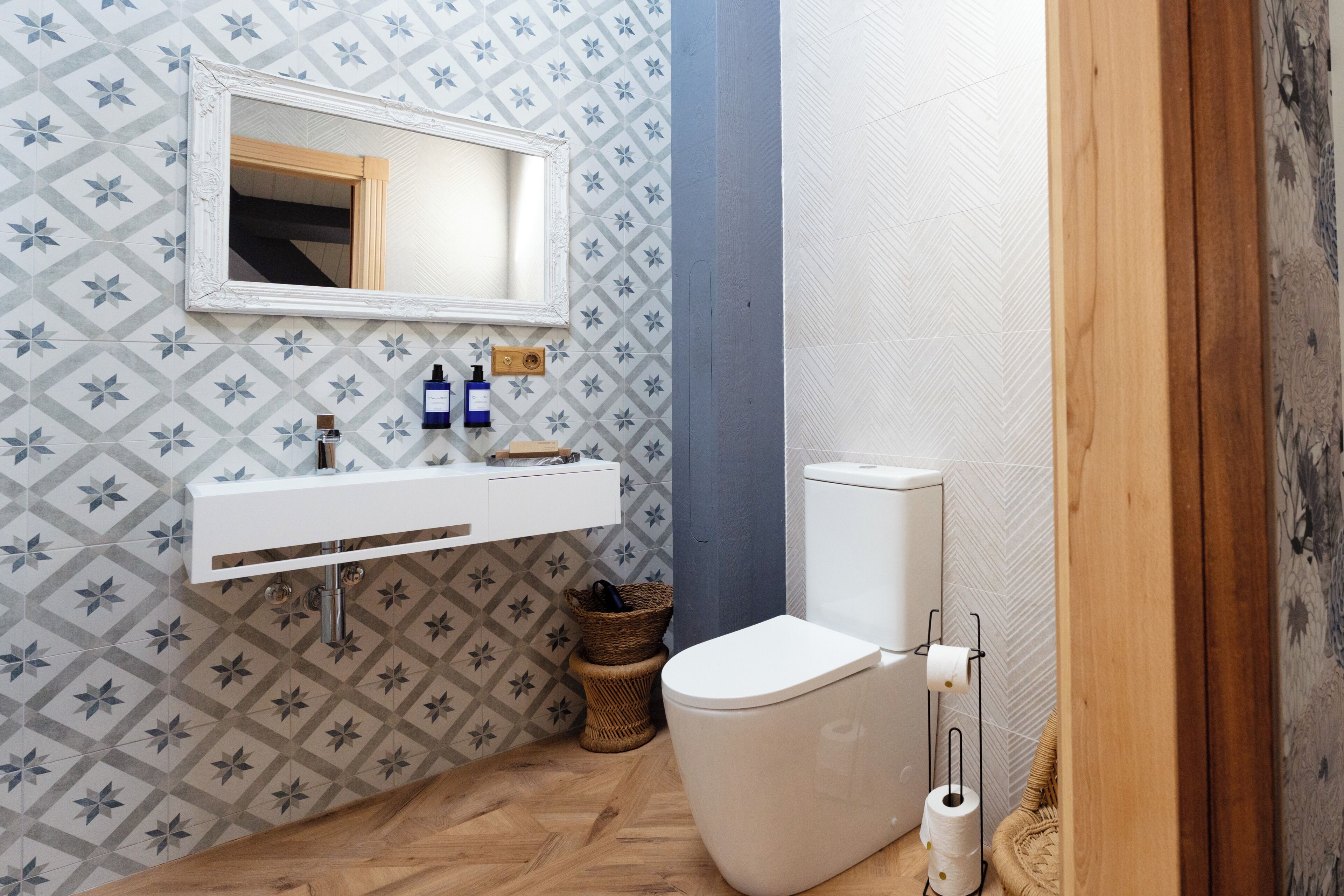 Een badkamer met een behang, een witte wastafel, een spiegel, een toilet en een mand.