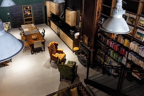 A room with a dining table, chairs, a sofa, a bookshelf, and a hanging light fixture.