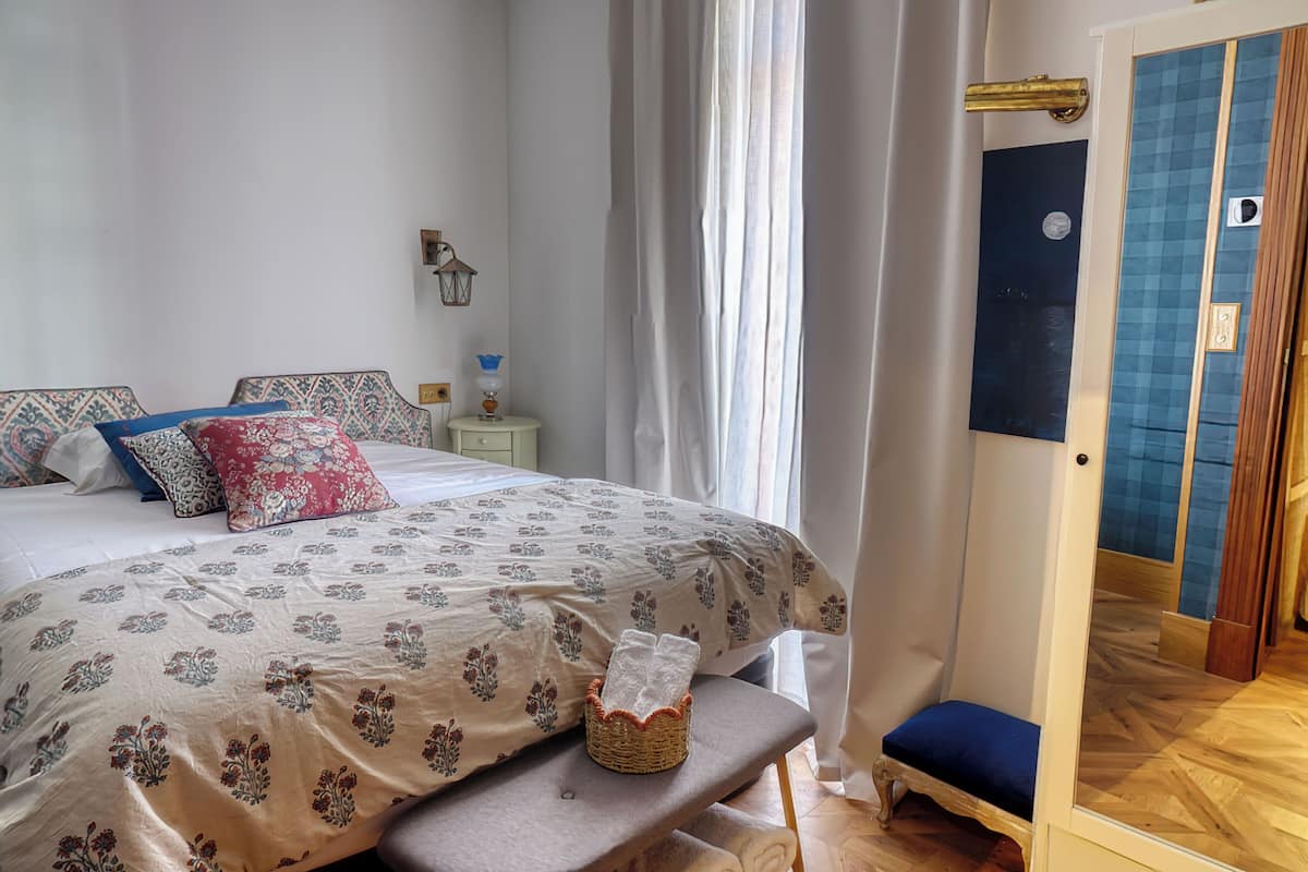 A bedroom with a bed, bedside table, lamp, and a small bench.