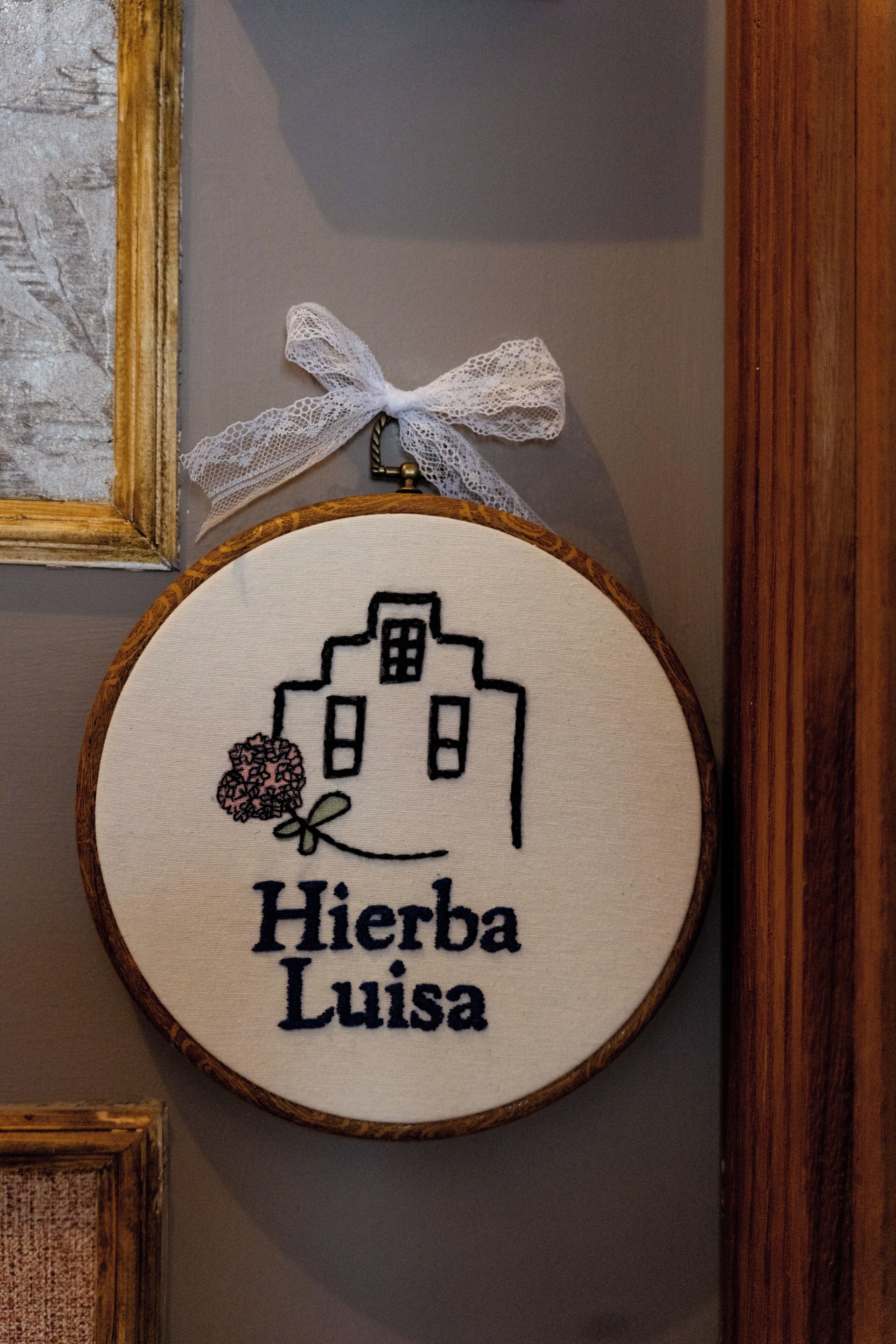 Un bordado circular que muestra un edificio y el texto 'Hierba Luisa' en una pared.