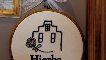 Un bordado circular que muestra un edificio y el texto 'Hierba Luisa' en una pared.