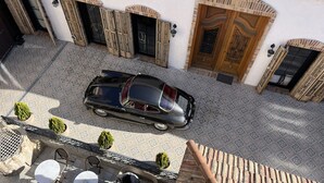 A black car parked on a patterned tile patio, with a building featuring arched windows and a wooden door in the background.