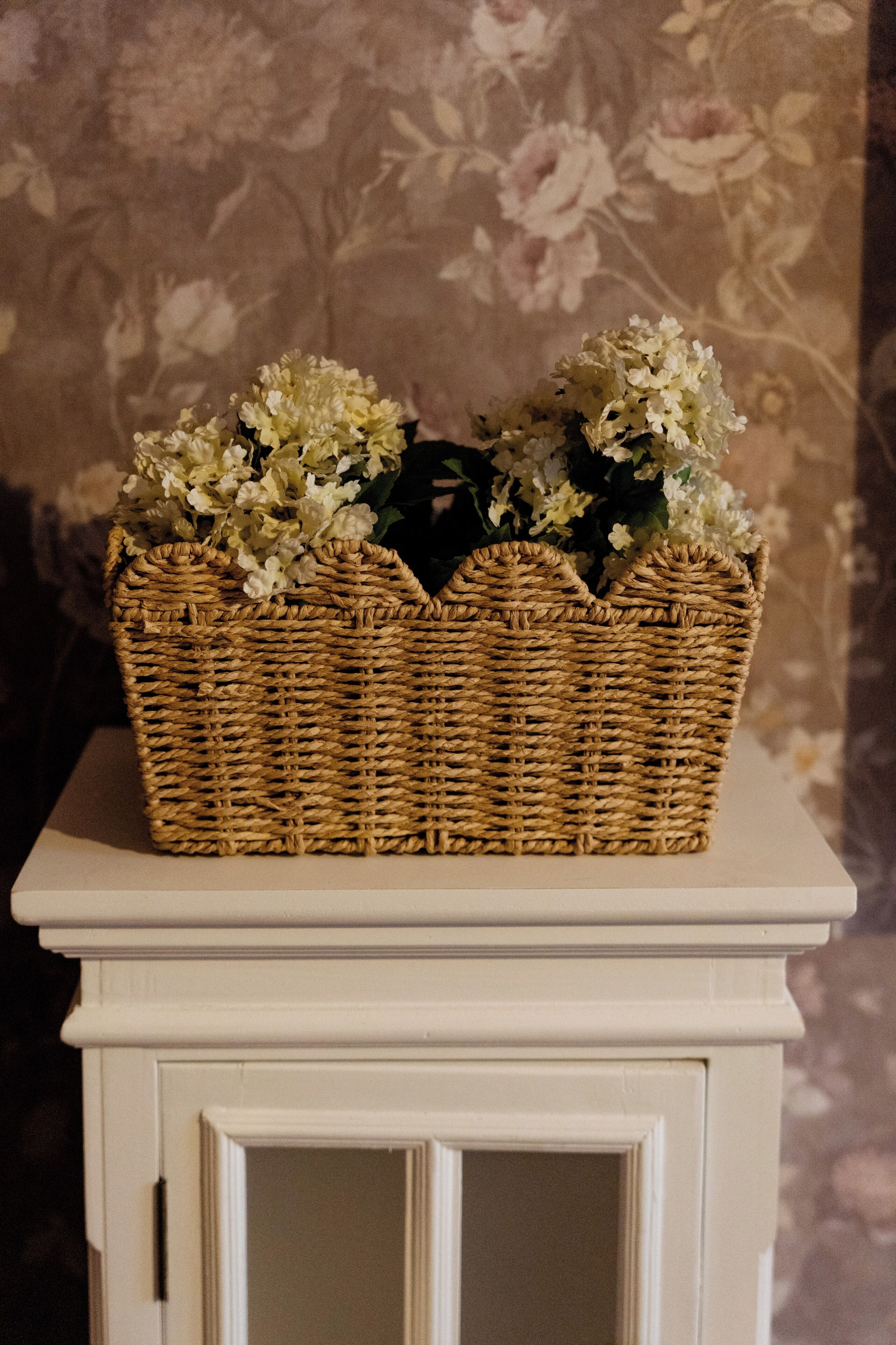 A wicker basket with flowers on a white cabinet.