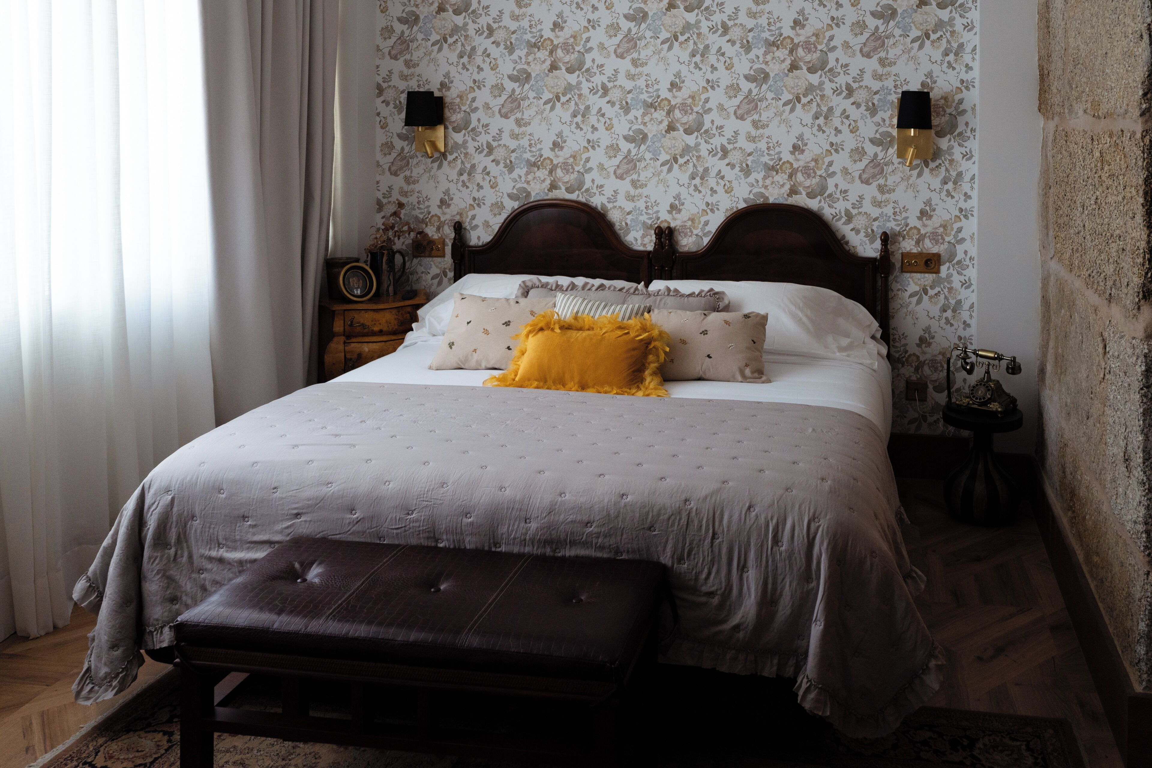 A bedroom with a wooden bed, a bench, a nightstand, and a wall-mounted lamp.