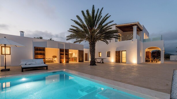 Ett modernt hus med en swimmingpool, en palm och en väl upplyst uteplats.