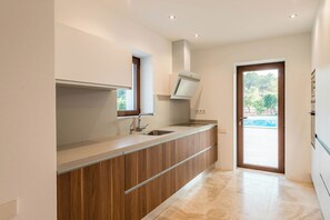 A modern kitchen with a built-in oven, a window, and a door leading to a balcony. - WHITE OASIS Ibiza Villa (Sant Llorenc de Balafia)