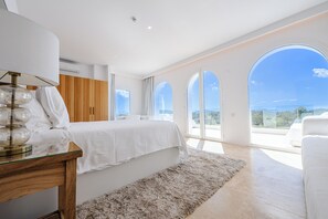 A modern bedroom with a large bed, a glass table, and a view of the outdoors. - WHITE OASIS Ibiza Villa (Sant Llorenc de Balafia)