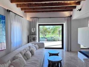 A modern living room with a sofa, two round tables, a cabinet, and a large window with a view of greenery. - WHITE OASIS Ibiza Villa (Sant Llorenc de Balafia)