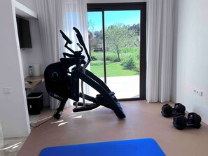 A home gym with an elliptical, dumbbells, and a yoga mat. - WHITE OASIS Ibiza Villa (Sant Llorenc de Balafia)