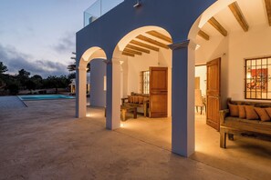 A covered outdoor area with a pool, wooden furniture, and a wooden door. - WHITE OASIS Ibiza Villa (Sant Llorenc de Balafia)