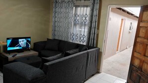 A living room with a sofa, a TV, and a patterned curtain. - Zondiles Guesthouse  (MP)