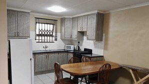 A compact kitchen with a dining area, featuring cabinets, a refrigerator, a microwave, and a stove. - Zondiles Guesthouse  (MP)