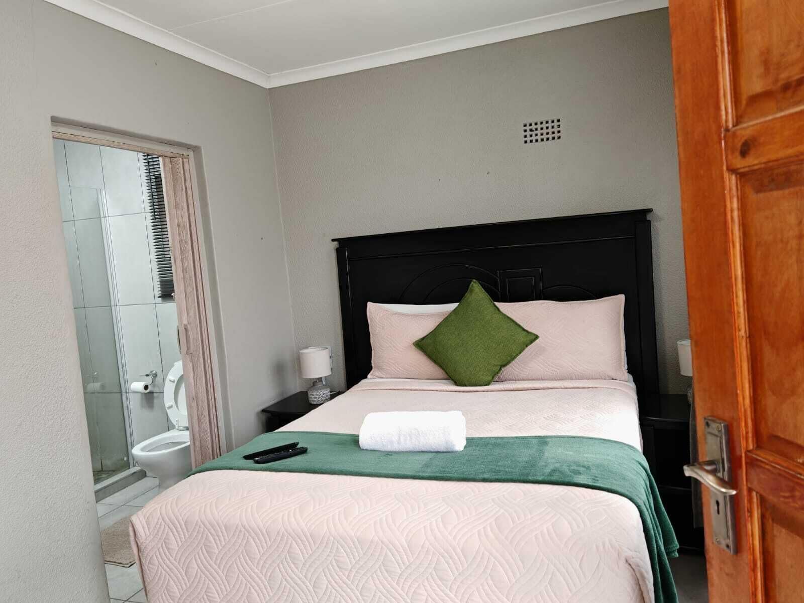 A hotel room with a bed, a nightstand, a green towel, a remote control, and a bathroom with a toilet and shower.